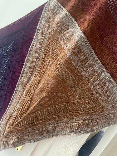 Three overlapping knitted shawls; foreground triangular brown-orange lace and textured shawl.