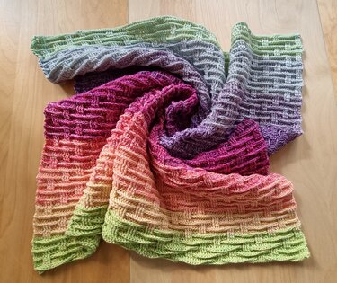 Multicolor gradient crocheted baby blanket with textured basketweave stitch draped on wooden table