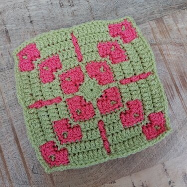 Zweifarbiges Häkel-Granny-Quadrat in Grün und Pink auf Holzuntergrund