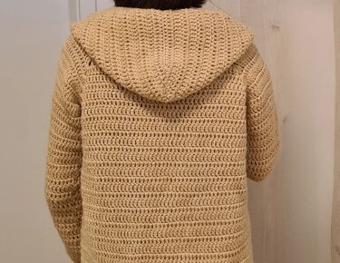 Rückenansicht einer beige gehäkelten Damenjacke mit Kapuze