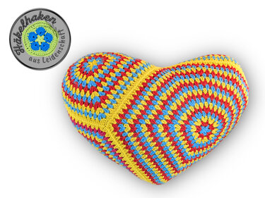 Gehäkeltes Herz-Kissen mit Granny-Hexagon-Muster in Gelb, Rot und Blau auf weißem Hintergrund