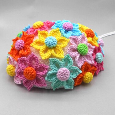 Crocheted egg-shaped decoration covered in colorful crochet flowers with pom centers on a neutral background