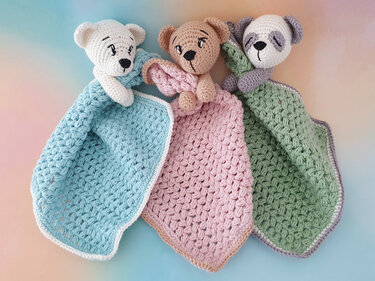 Three pastel crochet baby snuggle blankets in blue, pink, and green, each topped with a small bear or panda head.