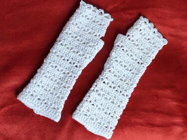 Zwei weiße fingerlose Armstulpen mit Häkel-Lochmuster auf rotem Stoff