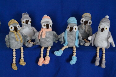 Mehrere winterliche Amigurumi-Eulen in Grau mit bunten Mützen und Schals auf blauem Hintergrund