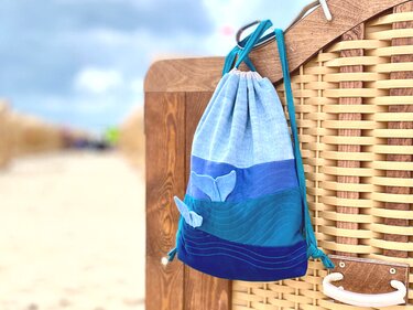 Blue drawstring bag with whale tail appliqués hanging on a wooden beach chair