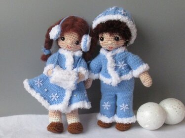 Zwei Amigurumi-Puppen in hellblauen Winteroutfits mit weißem Flauschrand und Schneeflockendekor.