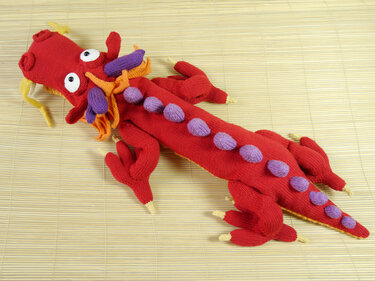 Red knitted amigurumi dragon toy with rounded purple spines, yellow accents and white eyes