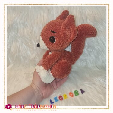 Gehäkeltes rotbraunes Eichhörnchen-Amigurumi mit weißer Schnauze und buschigem Schwanz, sitzend auf einer Hand