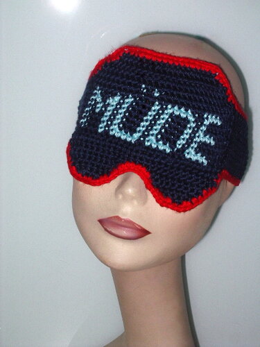 Gehäkelte dunkelblaue Schlafmaske mit rotem Rand und hellblauem Schriftzug 'MÜDE' auf einer Schaufensterpuppe.