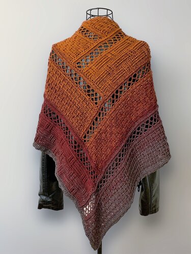 Triangle crochet shawl in ombre tones from orange to deep red to grey with lace-like openwork and textured stitches, draped over a dark jacket.