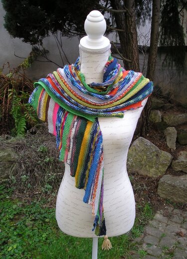 Gestricktes Dreieckstuch in Regenbogenfarben mit Streifen auf einer Schneiderpuppe im Freien.