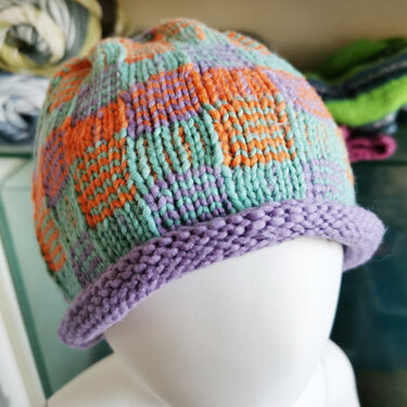 Pastellfarbene gestrickte Mütze mit Blockmuster und aufgerolltem Rand auf Mannequin-Kopf