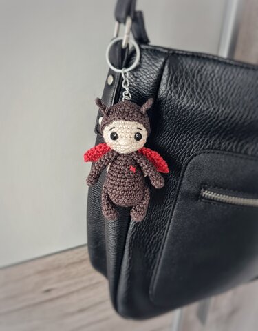 Gehäkelter Marienkäfer-Schlüsselanhänger mit braunem Körper und roten Flügeln an schwarzer Ledertasche