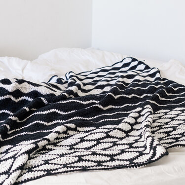Schwarz-weiße gehäkelte Decke mit dynamischem Wellenmuster auf weißem Bett