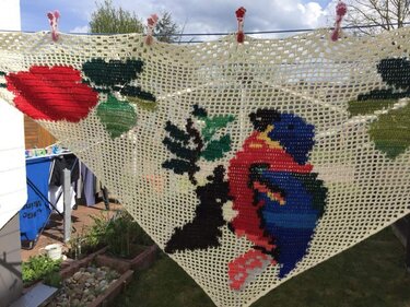 Dreieckiges gehäkeltes Motivtuch mit buntem Papagei und Blüten an einer Wäscheleine