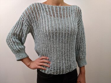 Person trägt mintgrünen, locker gestrickten Pullover mit weitem U-Boot-Ausschnitt und Dreiviertelärmeln.