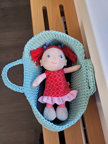 Hellblauer gehäkelter Korb mit Henkeln als Puppenbett für eine rothaarige Stoffpuppe.