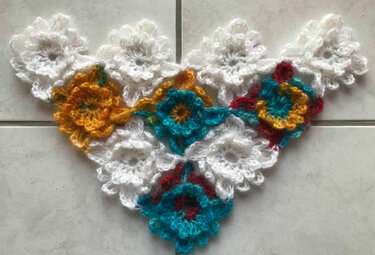 Gehäkeltes Dreieckstuch aus weißen und bunten Blumenmotiven auf hellem Fliesenboden