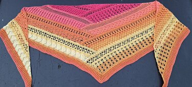 Crocheted triangle shawl with ombre pink, orange and yellow bands showing several distinct stitch textures.