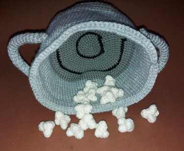 Gehäkelter hellblauer Popcorn-Eimer mit lächelndem Gesicht und weißen Popcorn-Stücken