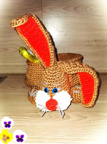 Gehäkelter brauner Osterhase mit roten Ohrinnenflächen, blauen Augen und Rückfach mit eingewickelter Süßigkeit.