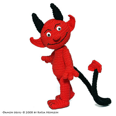 Rote gehäkelte Amigurumi-Teufelsfigur mit schwarzen Hörnern und langem Schwanz, stehend