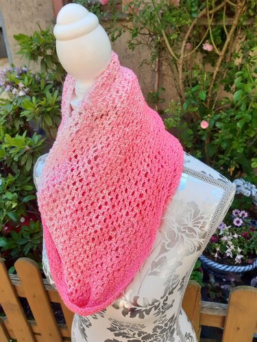 Handgehäkelter Loop-Schal in Pink-Ombre mit offenem Lochmuster auf einer Schaufensterpuppe im Garten