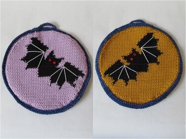 Zwei runde gehäkelte Topflappen: links lila mit schwarzer Fledermaus, rechts senfgelb mit schwarzer Fledermaus, beide mit blauem Rand und Aufhängeschlaufe.