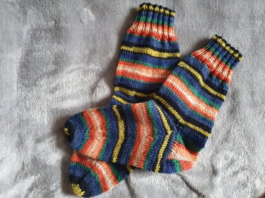Ein Paar gestrickte Damensocken mit horizontalen Streifen in Blau, Orange, Gelb und Grün auf grauer Decke