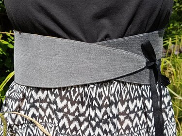 Grauer Wickelgürtel mit spitzer Blende, sichtbarer Naht und schwarzer Schleife am Bund