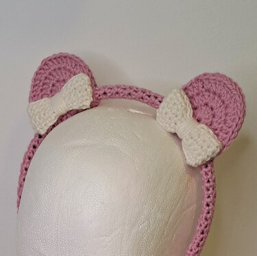 Rosa gehäkeltes Kinderstirnband mit zwei Katzenohren und weißen Schleifen