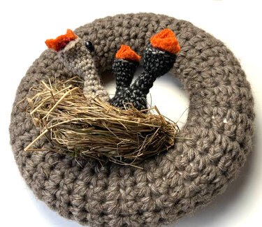 Gehäkelter runder Türkranz in Naturgrau mit Stroh‑Nest und drei dunklen Stängeln mit orangefarbigen Spitzen