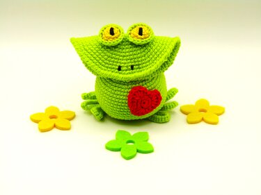 Gehäkelter grüner Frosch-Amigurumi mit rotem Herz und Deko-Blumen