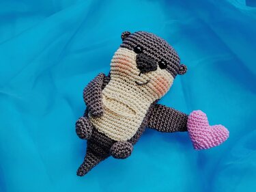 Gehäkeltes Otter-Amigurumi auf blauem Stoff mit rosa Herz