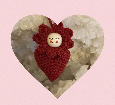 Roter, gehäkelter Amigurumi-Anhänger in Erdbeerform mit Holzperlen-Gesicht und Blütenkranz vor hellem Hintergrund