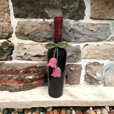 Dunkle Flasche mit gehäkelter grüner Schleife und zwei rosa glockenförmigen Anhängern