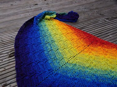 Gehäkeltes Dreieckstuch mit Regenbogen‑Farbverlauf auf Holzterrasse