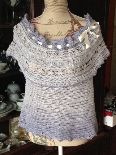 Gehäkeltes Damen-Top in Grau-Lila mit weitem U-Boot-Ausschnitt, Lochmuster und Schleifenband auf einer Schneiderpuppe.