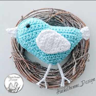 Pastellblauer Amigurumi-Vogel mit weißen Flügeln im Naturkranz