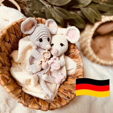 Zwei gehäkelte Amigurumi‑Mäuse (grau und cremeweiß) mit kleinen Blüten in einem geflochtenen Korb