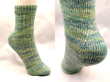 Grün-blau melierte handgestrickte Socke auf Fußmodell, Seiten- und Fersendetail sichtbar.