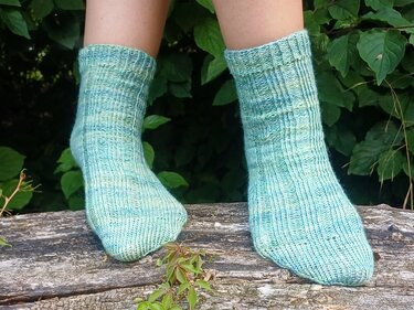 Mintgrüne, gestrickte Kurzsocken mit Rippenmuster an Beinen vor grünem Laub
