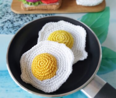 Small crocheted fried eggs showing stitch texture in a frying pan