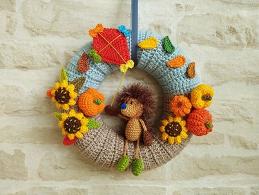 Gehäkelter Herbstkranz mit Igel, Flugdrachen, Sonnenblumen und Kürbissen an einer Wand