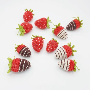 Assortment of handmade crocheted strawberries, including plain red and striped dipped-style versions, on a white background.
