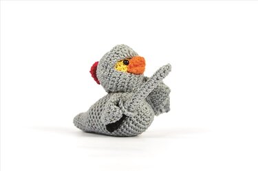 Grau gehäkelte Amigurumi-Ente im Ritterkostüm mit orangefarbenem Schnabel und kleinem Schwert