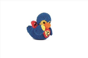 Gehäkelte Amigurumi-Ente im blauen Superheldenkostüm mit rotem Umhang