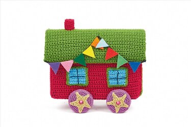 Gehäkeltes Amigurumi-Haus in Rot und Grün mit blauen Fenstern und bunter Filzwimpelkette auf lila Rädern