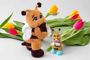 Zwei gehäkelte Bienen (groß und klein) mit Blumensträußen vor bunten Tulpen